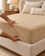 Hands fitting the beige Terry Mattress Protector over the mattress corner