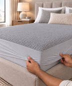 Hands fitting the grey Terry Mattress Protector over the mattress corner