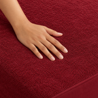 Adult hand gently touching the maroon Westy Home terry mattress protector, showing its fine unquilted loop texture and bound edge